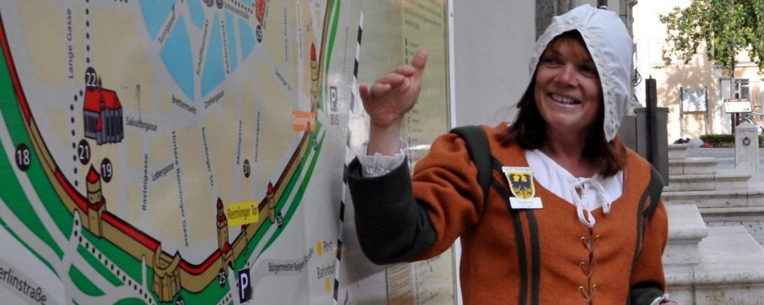 Auf diesem Bild sieht man die Gästeführerin Sonja Fall im historischen Gewand vor einem Stadtplan von Nördlingen.
