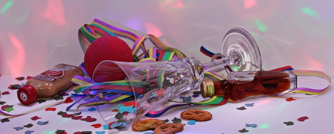 Das Bild zeigt ein Sektglas, Konfetti, einen Klopfer und eine Clownsnase. 