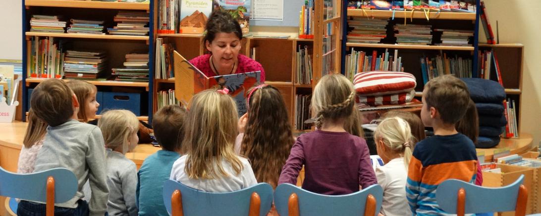 Das Bild zeigt eine Frau beim Vorlesen mit Kindern. 
