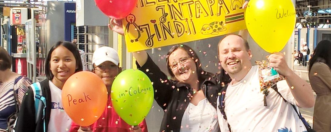 Gastfamilie und Austauschschüler stehen zusammen am Bahnhof. 