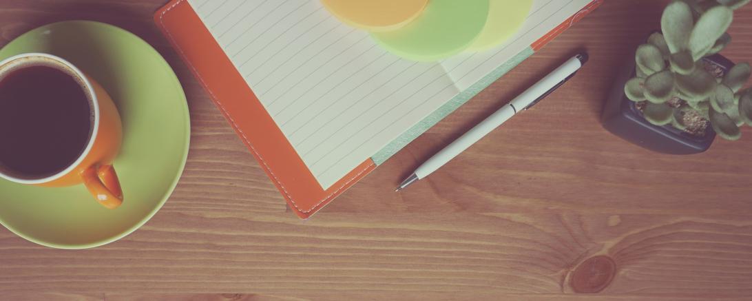 Auf dem Tisch steht eine Kaffeetasse, eine Blume und ein Block. 