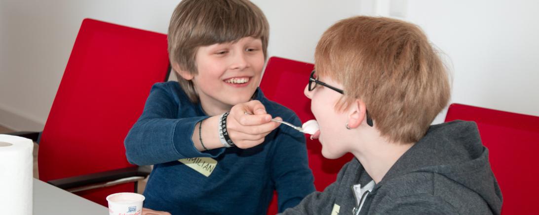 Das Bild zeigt Maximilian und Tim beim gegenseitigen Joghurteingeben.
