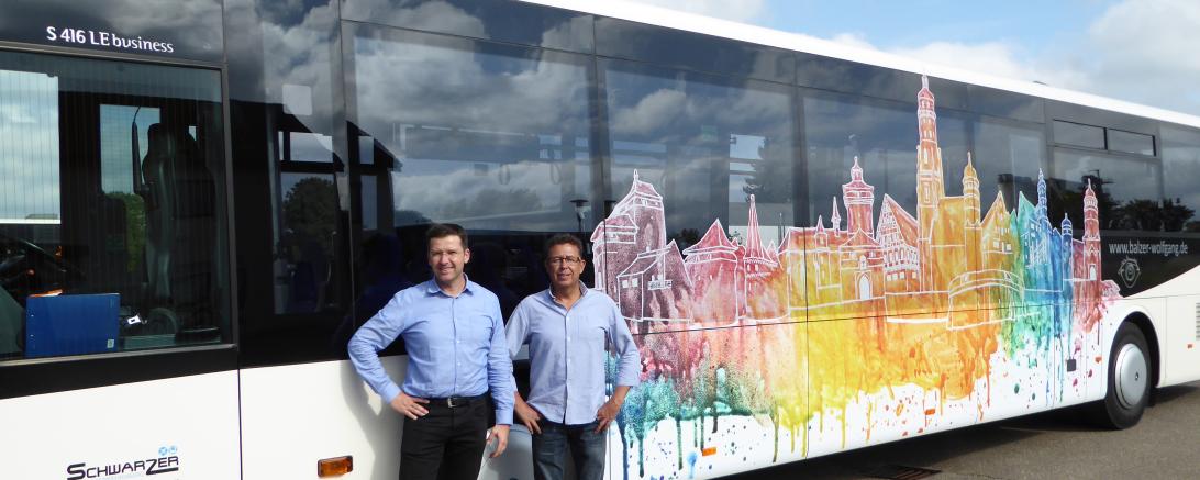 Das Bild zeigt den Künstler Wolfgang Balzer und Verkehrsunternehmer Jörg Schwarzer vor dem Linienbus mit dem Kunstwerk der Nördlinger Stadtsilhouette