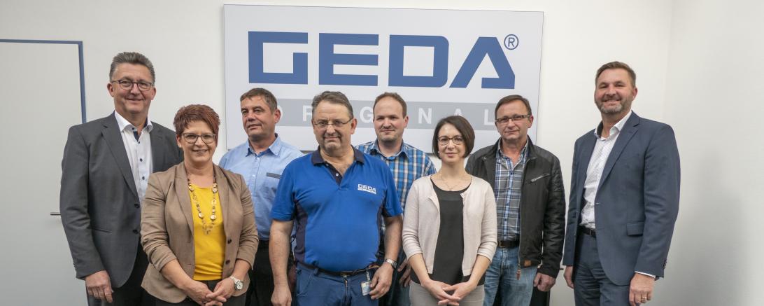 Das Bild zeigt langjährige Mitarbeiter der Firma Geda bei ihrer Ehrung dazu.