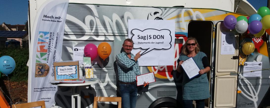 Das Foto zeigt den Vorsitzenden der CID, Markus Sommer, und Stadtjugendpflegerin Daniela Benkert vor dem Wohnwagen, der bei der Kunst- und Lichternacht diesen Samstag in der Spitalstraße stehen wird, für Kurzstatements der Jugendlichen.