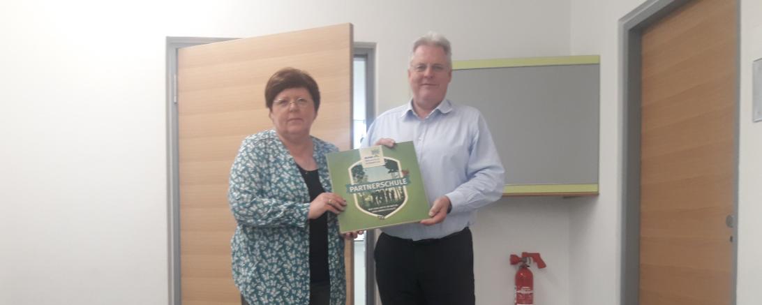 Erika Wiedemann, die Organisatorin der Haussammlung überreicht Schulleiter Robert Böse die von Alexander Helber, dem 1. Vorsitzenden BN Donau-Ries, erhaltene Auszeichnung. 