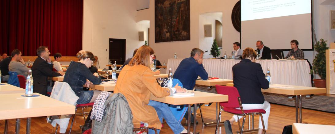 Stadträte sitzen verteilt an Tischen vor Podium