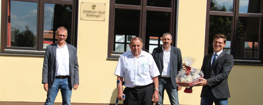 Vier Männer stehen vor Goldbachsaal Baldingen, einer mit Präsentkorb