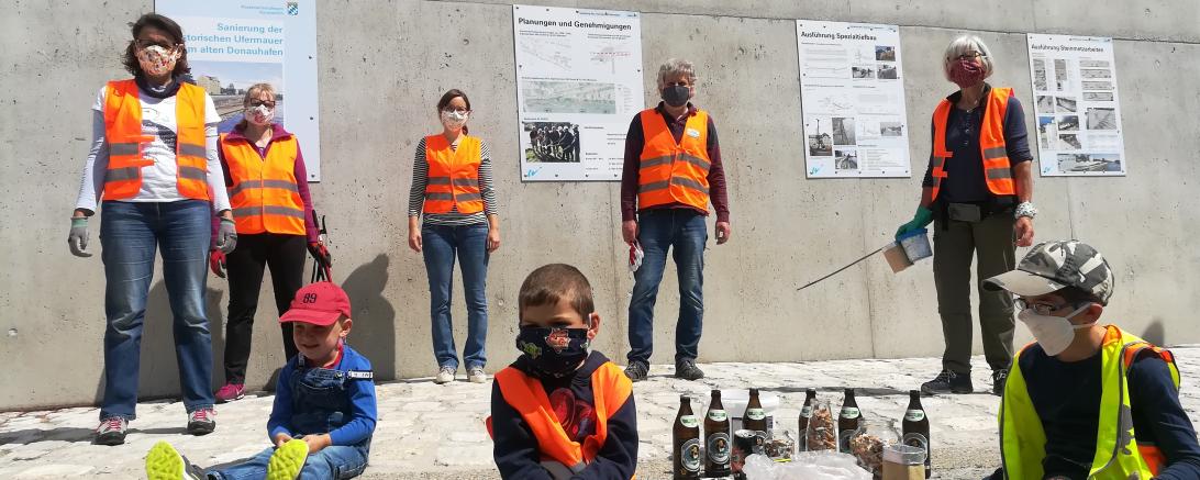 Fünf Erwachsene und drei Kinder mit Masken und Warnwesten vor Ufermauer Donauwörth