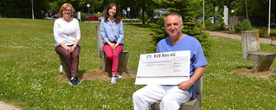 Drei Personen sitzen auf Wiese, Mann mit Scheck