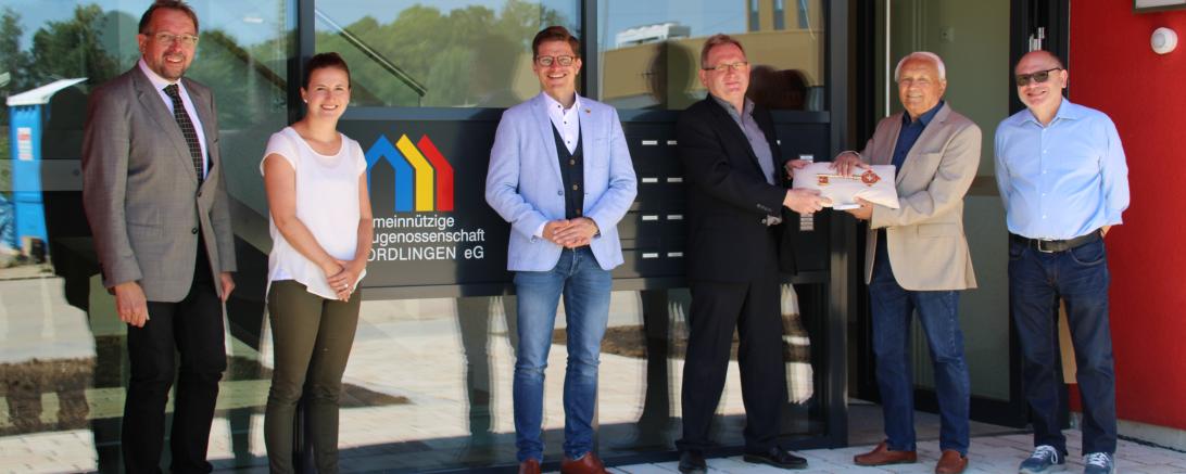 Sechs Personen mit goldenem Schlüssel vor Eingang eines Mehrfamilienhauses