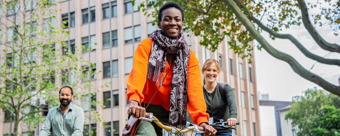 Drei lachende Personen auf Fahrrädern vor Wohnhaus