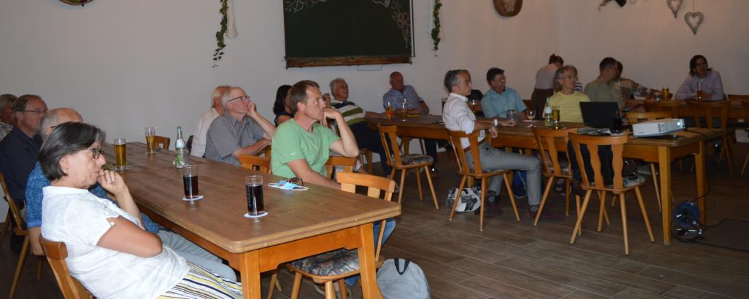 Personen sitzen im Wirtshaus und hören einen Vortrag