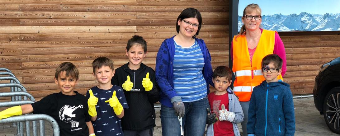 Fünf Kinder und zwei Frauen mit Handschuhen und Müllsammelwerkzeug