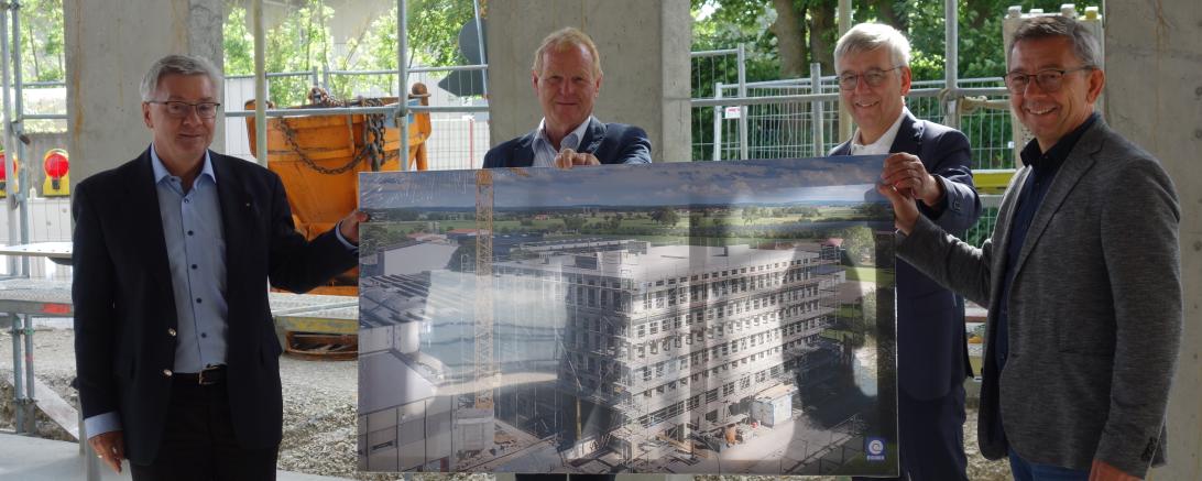 Vier Männer in Rohbau mit großem Bild des Gebäudes