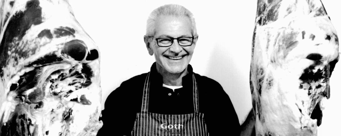 Wolfgang Göth mit Metzgerschurz zwischen zwei Schweinehälften, in schwarz-weiß