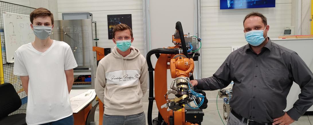 Drei Herren mit Masken und Fertigungsroboter