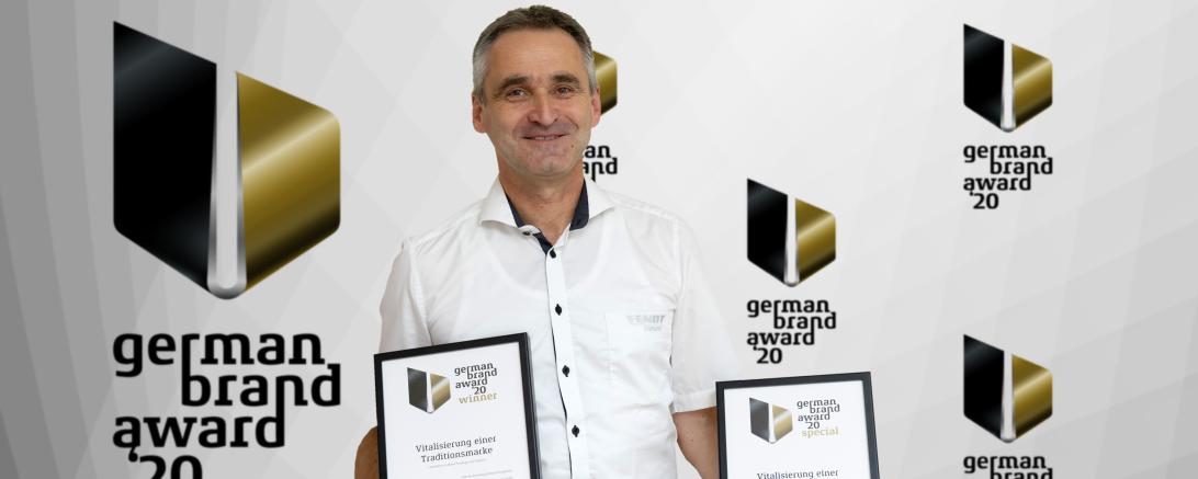 Mann mit zwei Urkunden vor Wand mit Logo "German Brand Award"