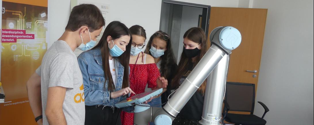 Mädchen mit Schutzmasken lassen sich Roboterarm erklären