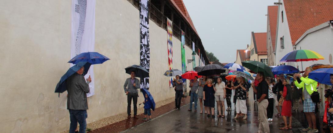 Fahnen an Nördlinger Stadtmauer, davor Publikum mit Regenschirmen