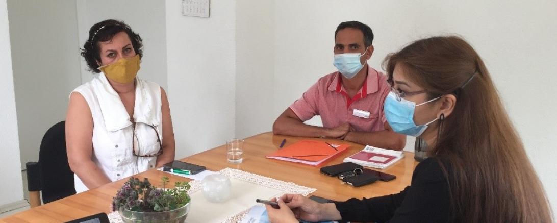 Drei Personen mit Mundschutz sitzen an einem Tisch