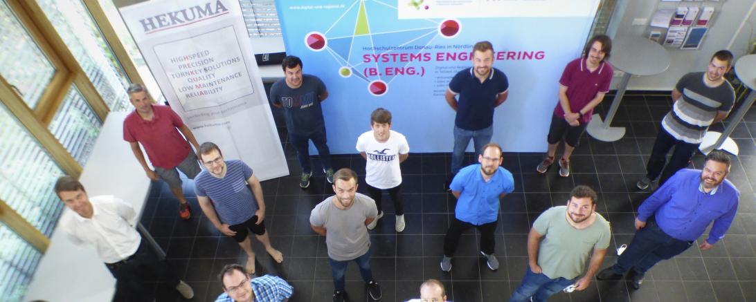 Studenten stehen in Raum vor Roll-ups, mit Abstand