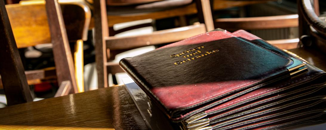 Das Bild zeigt ein leeres Restaurant und Speißekarten auf einem Tisch liegen