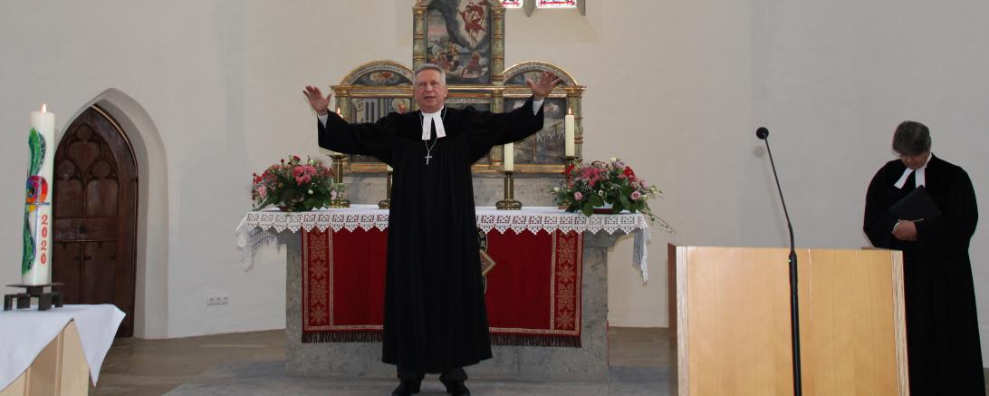 Pfarrer im Talar steht in Kirche vor Altar, Arme ausgebreitet