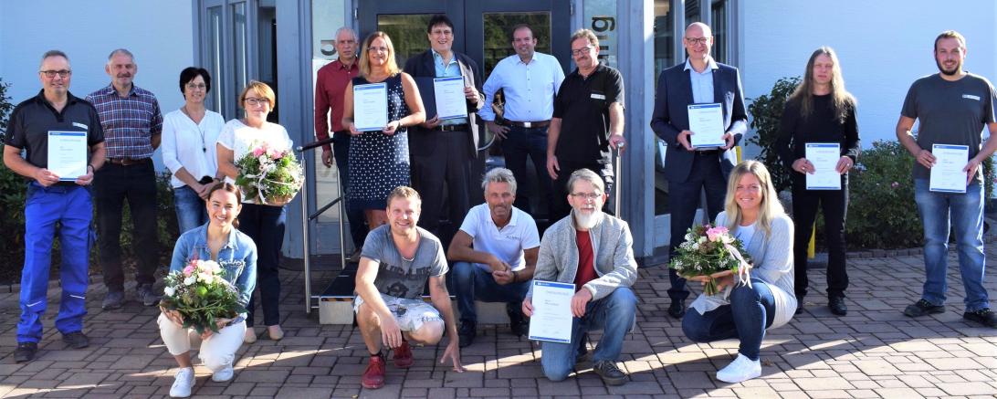 17 Personen mit Urkunden bzw. Blumensträußen stehen bzw. knien vor JELD-WEN-Eingang