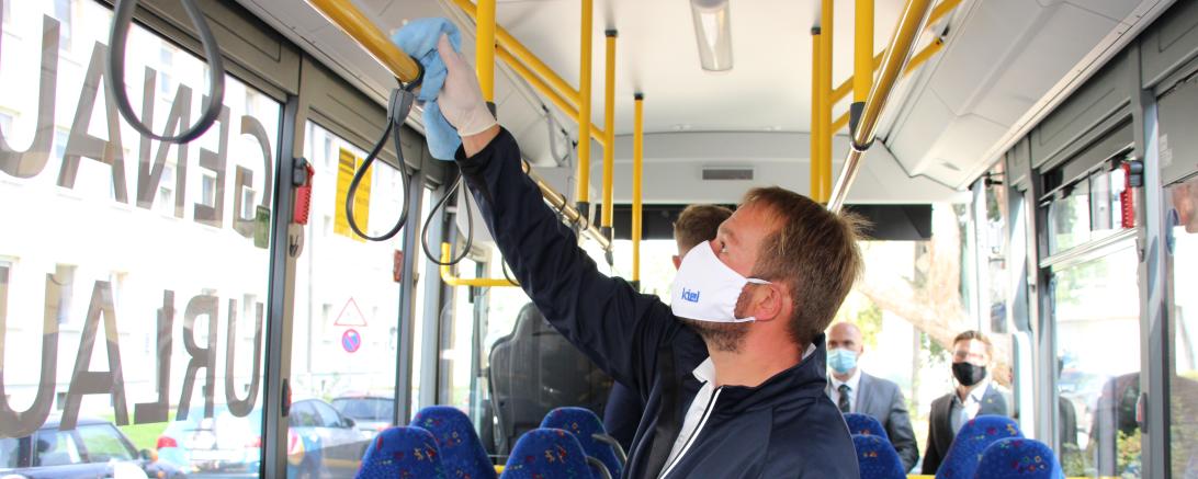 Mann mit Maske trägt Virenschutzschicht auf Haltestange in einem Bus auf