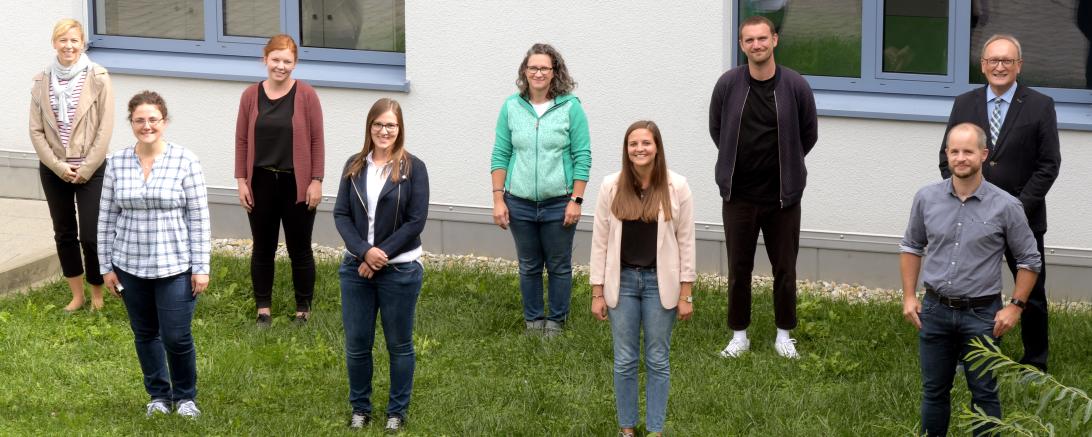 Neun Personen stehen mit Abstand vor Schulgebäude