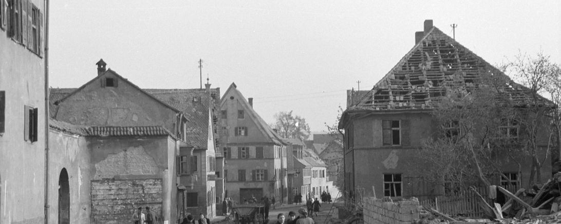 April 1945: Ein Blick in die zerstörte Pflegstraße in Donauwörth mit Passanten, gegenüber dem Fuggerhaus auf der linken Seite liegen die Trümmer des zerstörten Eckhauses. 
