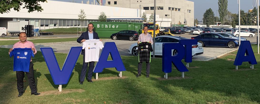 Drei Männer mit Trikots bei Logo der Varta AG