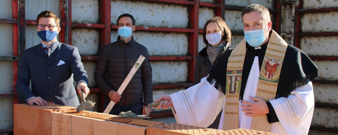 Vier Personen mit Maske legen Grundstein auf Baustelle
