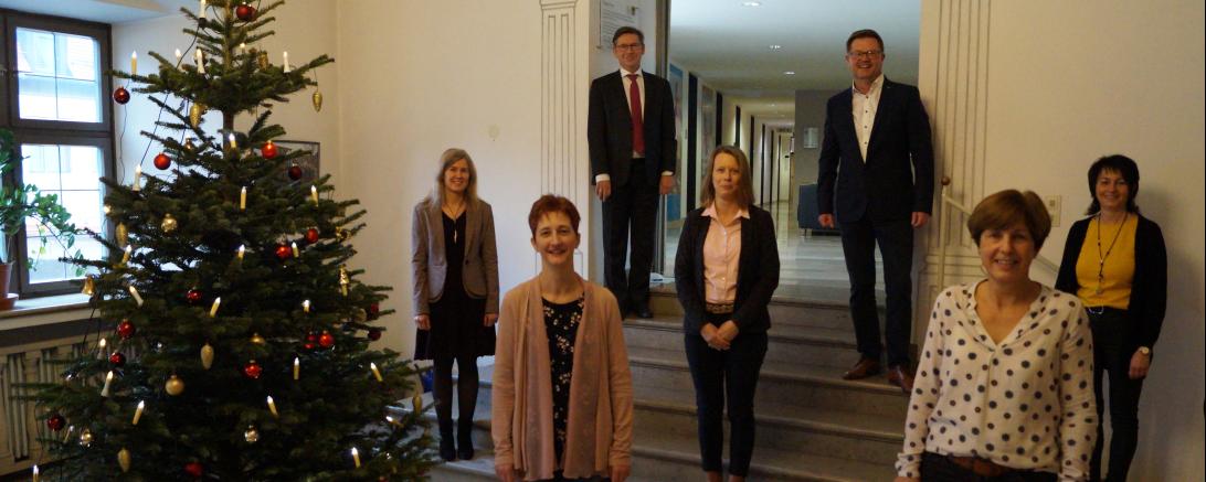 Sieben Personen stehen mit Abstand neben einem Weihnachtsbaum