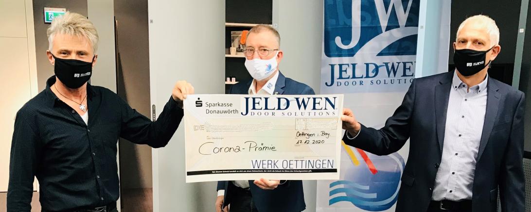 Drei Männer mit Mundschutz und Scheck vor Jeld-Wen-Banner