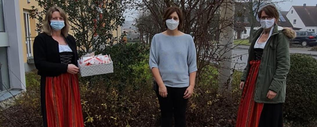 Drei Frauen mit Masken, zwei davon in Tracht