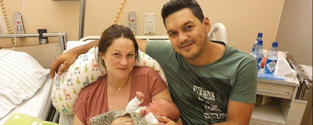 Mutter und Vater mit Neugeborenem in Krankenhausbett