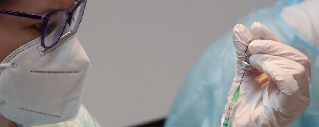 Ärztin mit Mund-Nasen-Schutz zieht Spritze auf