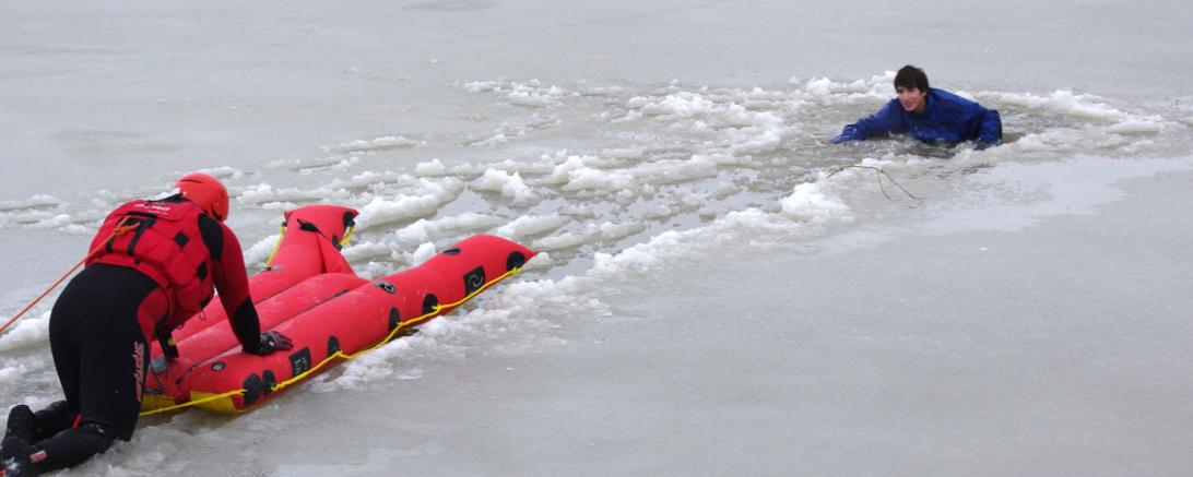 Das Bild zeigt einen Retter der DLRG, der sich mit einem aufblasbaren Eisrettungsschlitten zu einer eingebrochen Person vorarbeitet.