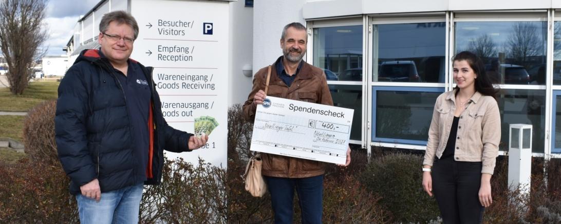 Drei Personen mit Scheck vor SPN Firmensitz