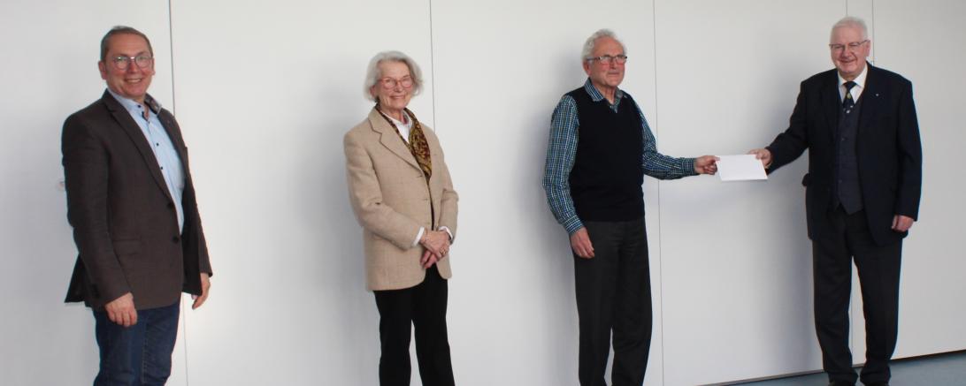 Vier Personen vor weißer Wand bei Spendenübergabe