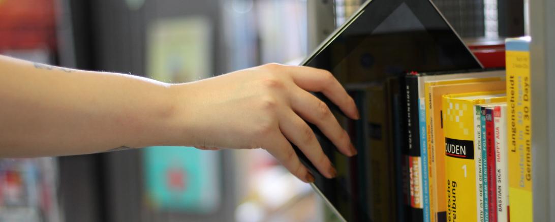 Das Bild zeigt ein Tablet in einem Bücherregal. 