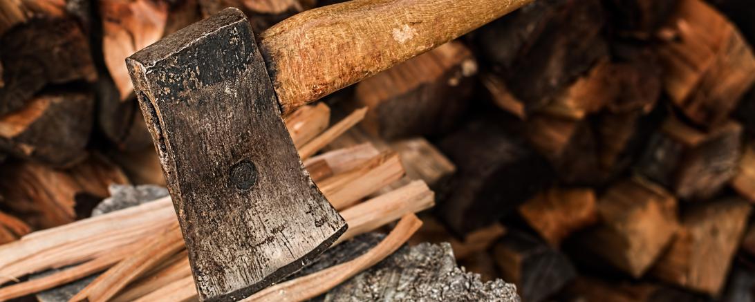 Handaxt auf Hackblock, dahinter Holzscheite
