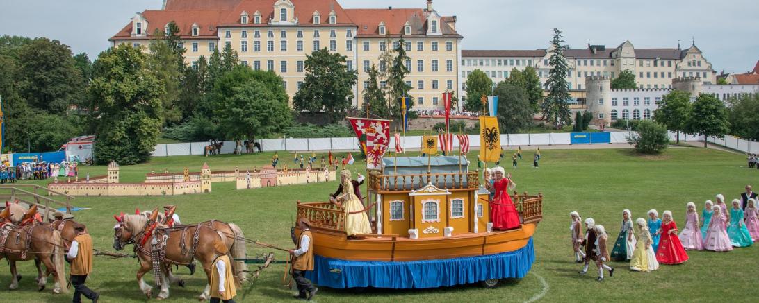 Das Bild zeigt eine Parade von Menschen, die mit barocken Kleidern anzogen sind.