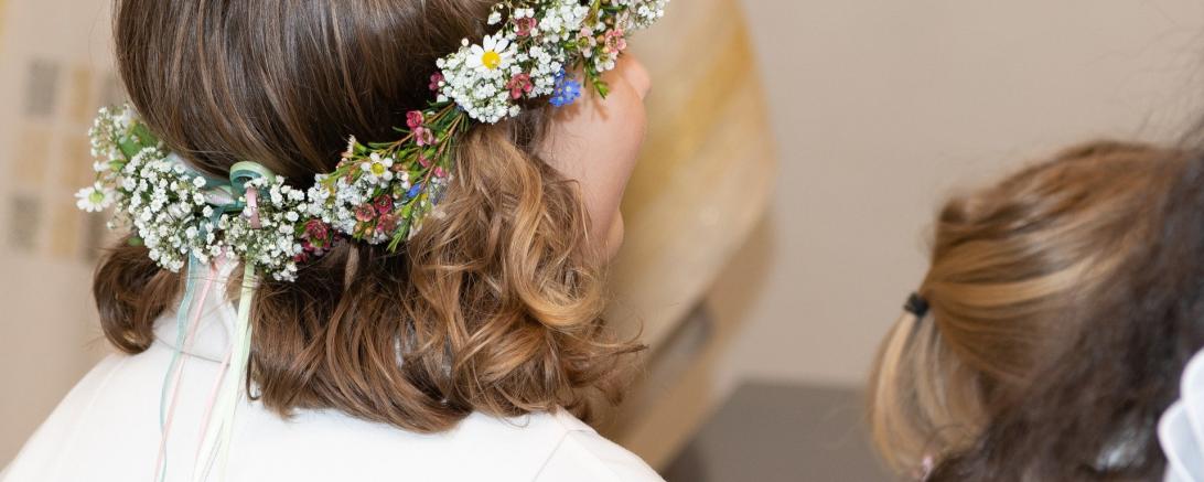 das Bild zeigt ein Mädchen von hinten mit einem Blumenkranz auf dem Kopf. 