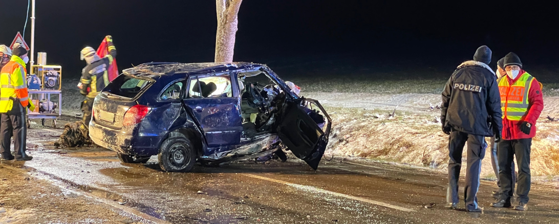 Unfallwagen steht auf Straße, dabei Polizisten und Feuerwehrleute