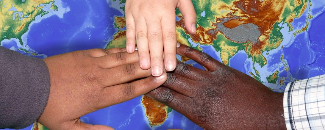 Das Bild zeigt mehrere Händen von verschiedenen Hautfarben, die sich in der Mitte des Bildes berühren.