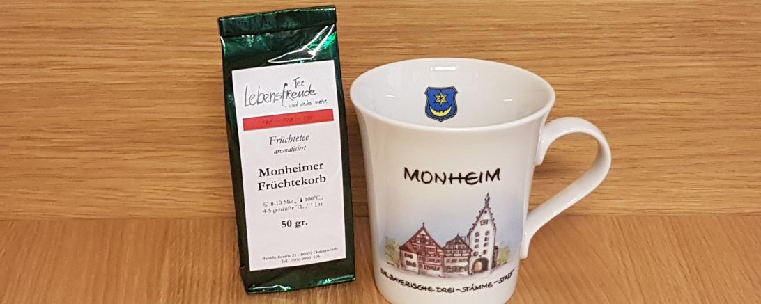 Das Bild zeigt eine Tasse mit dem Motiv von Monheim - daneben steht eine Tee-Mischung.