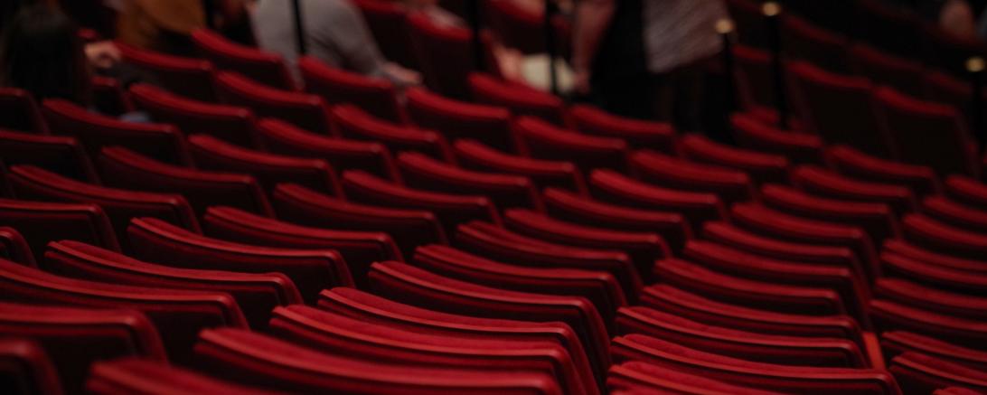 Das Bild zeigt mehrere Reihen von roten Theatersitzen.